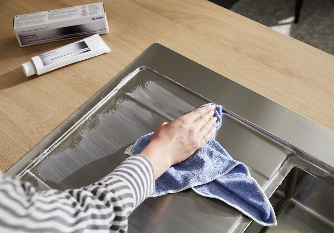 Hand poliert eine Edelstahlspüle mit Mikrofasertuch, daneben BLANCO DeepClean