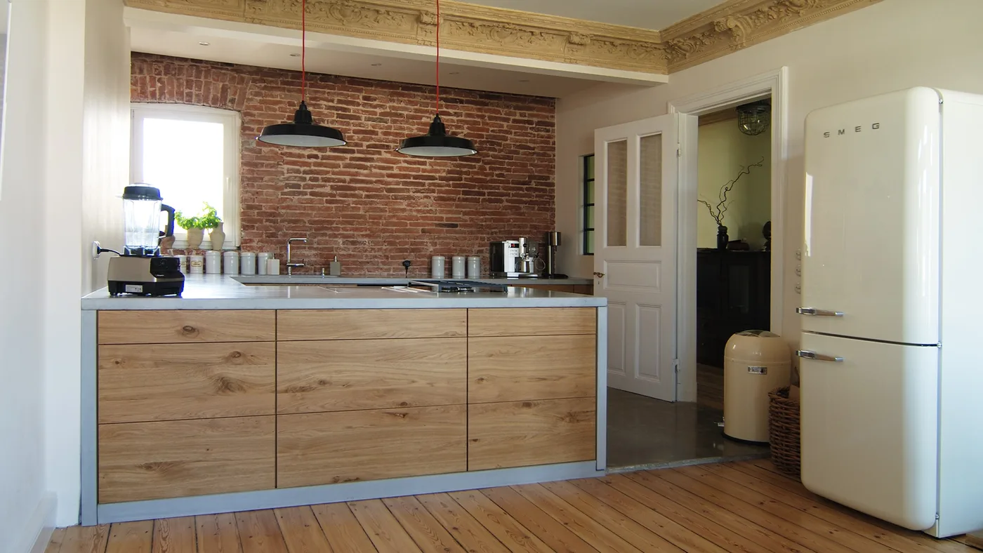 Loftküche mit heller Beton-Arbeitsplatte, Eichenfronten und Backsteinwand von material raum form