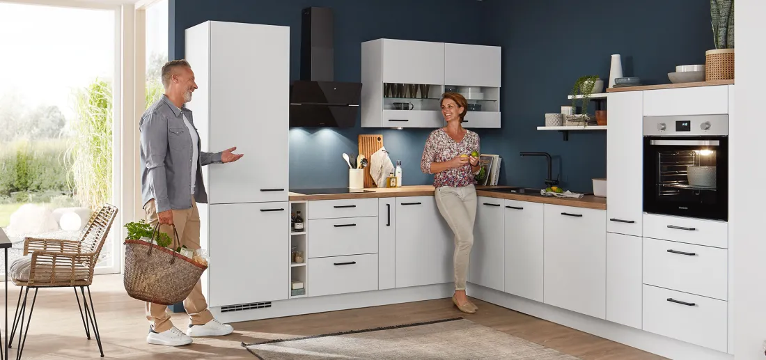 nobilia elements L-Küche in Weiß mit Holzarbeitsplatte und Hochschrank vor blauer Wand